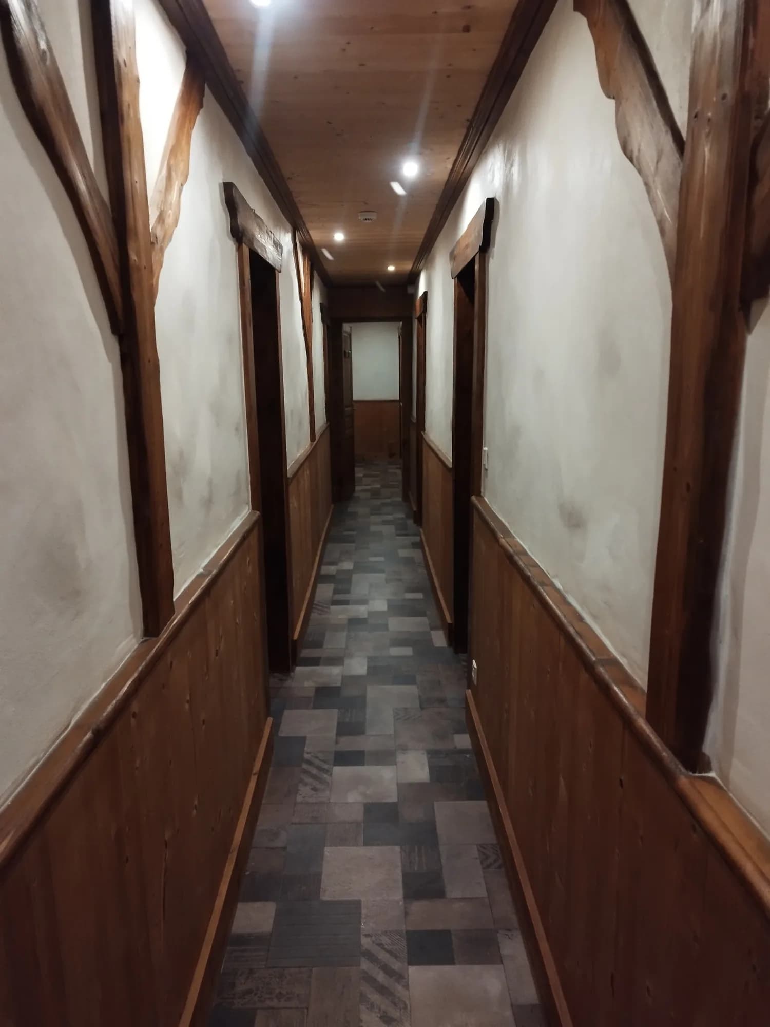 Couloir étroit lambrissé de bois desservant plusieurs chambres