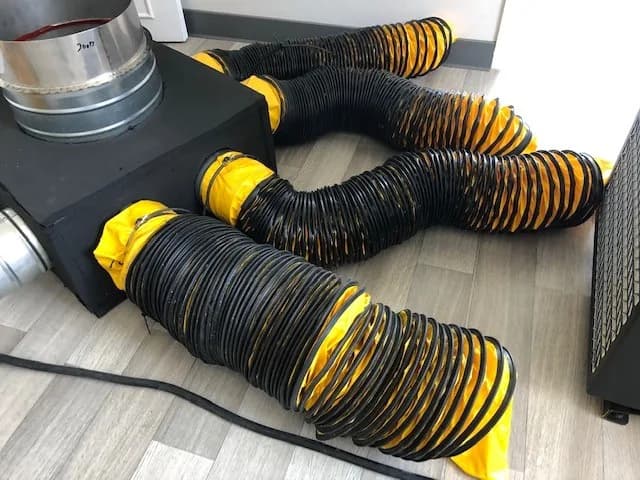 Caisson de répartition raccordé à plusieurs gaines souples jaune et noir déployées au sol d'une pièce