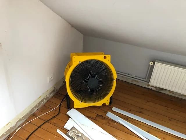 Chambre mansardée vidée de son mobilier, turbine de brassage posée au sol près d'un radiateur