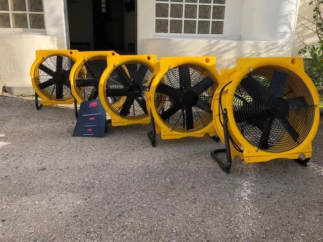 Cinq turbines de brassage d'air jaunes alignées devant l'entrée d'un bâtiment